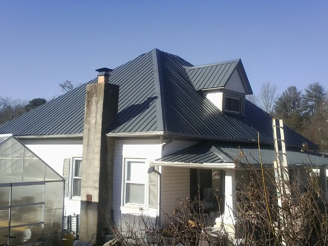 Dark blue standing seam metal roof on a white farmhouse with dormer — Slate & Tile Roof Repair by Roofing Brothers in Copper Hill