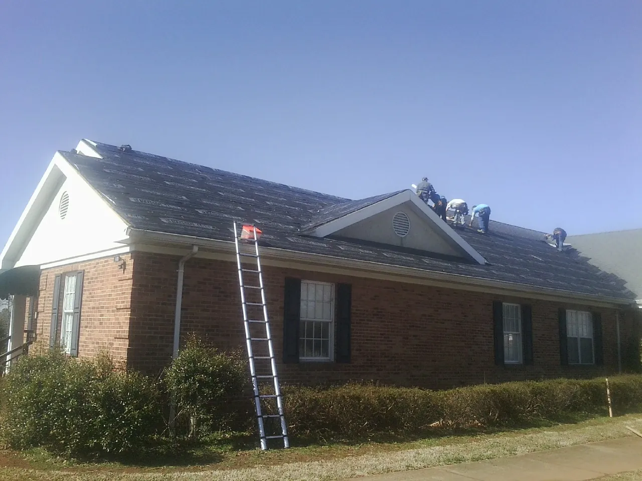 Crew tearing shingles off a brick ranch roof with a ladder set — Emergency Roof Repair work by our crew in Copper Hill