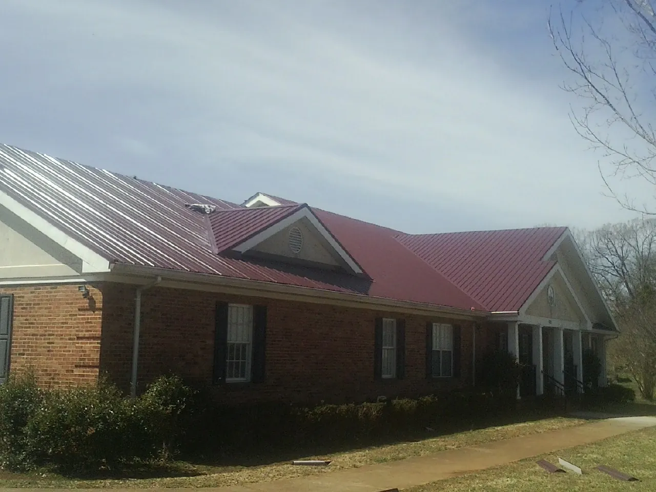 Red metal roof with gabled entries on a long brick building, from a Hail Damage Roof Repair job in Copper Hill