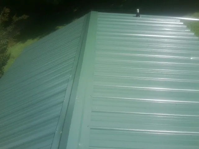 New green metal panels meeting at the ridge of a roof — Flat Roof Repair work by our crew in Copper Hill