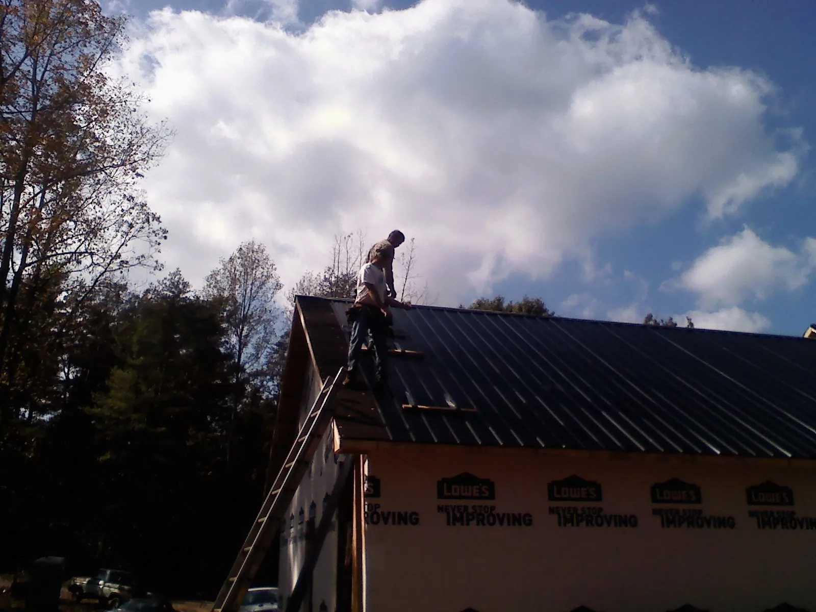 Roofer fastening dark metal panels high against a cloudy sky, from a Roof Inspection job in Copper Hill