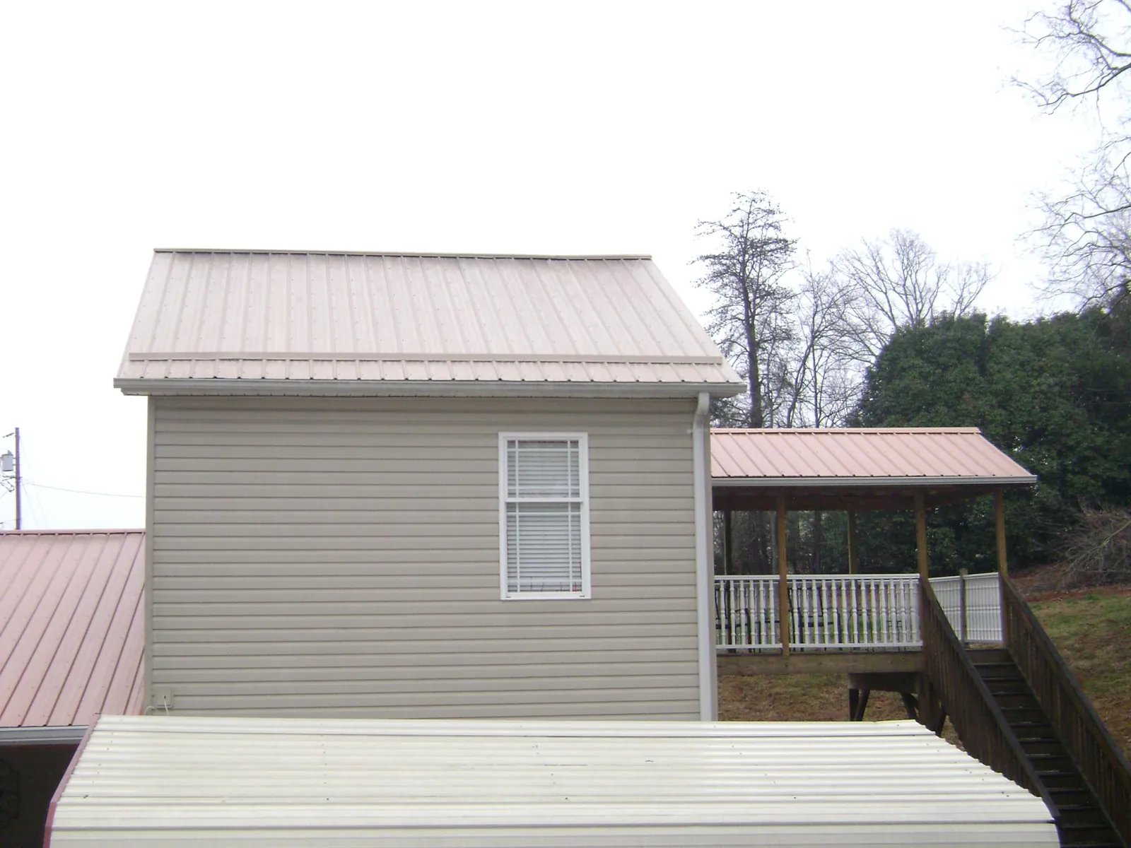 Tan metal roofs on a two story addition and attached porch, from a Roof Replacement job in Copper Hill